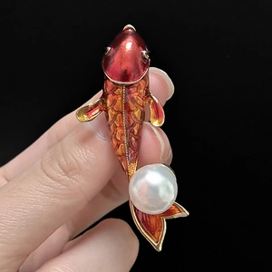 Macro detail of red enamel koi fish brooch with large white pearl on golden metal base