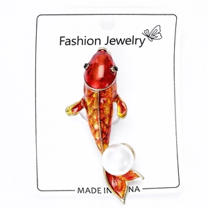 Detail of red enamel koi fish brooch with large white pearl on jewelry display card