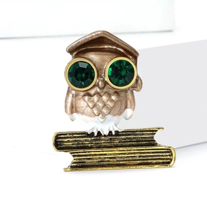 Vintage gold owl brooch with green gem eyes and academic cap on white platform