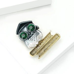 Detailed close-up of owl brooch featuring green gemstone eyes and gold book detail