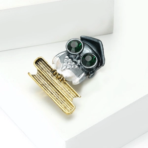 Detail of owl brooch featuring green crystal eyes and academic hat on white block