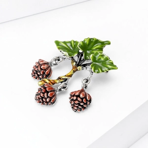 Elegant hazelnut fruit brooch with green enamel leaves on a minimalist white background