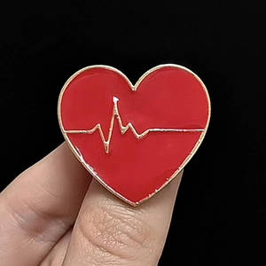 Primo piano di una spilla in smalto a forma di cuore con design ECG dorato in mano
