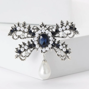 Detail of vintage silver bow brooch with deep blue gemstone and waterdrop pearl pendant