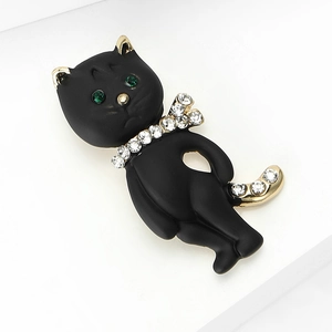 Eleganter schwarzer Katzen-Anstecker mit grünen Kristallaugen auf weißem minimalistischem Sockel
