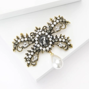 Vintage gold alloy bow brooch with white pearls and rhinestones on white background