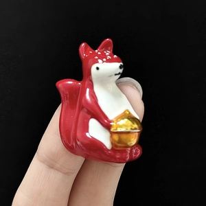 Vue macro d'une petite broche écureuil en céramique tenue par les doigts pour l'échelle