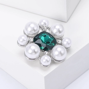 Détail macro d'une broche fleur élégante avec pierre émeraude carrée et perles blanches