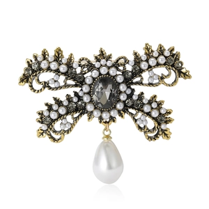 Vintage gold alloy bow brooch with white pearls and grey rhinestones on white background