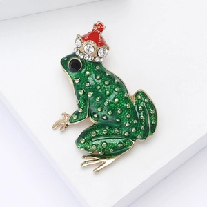 Broche émaillée grenouille avec peau verte et couronne dorée sur fond blanc épuré