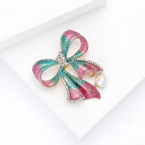 Détail d'une broche nœud papillon en cristal avec paillettes roses vertes et perle blanche