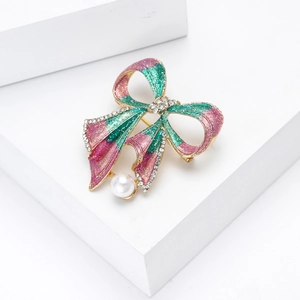 Détail d'une broche nœud étincelante avec émail rose, strass brillants et perle blanche