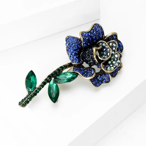 Macro shot of vintage rose brooch with blue crystals and green leaf details