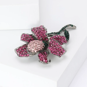 Detail view of pink and green crystal rose brooch with gunmetal finish on white stand