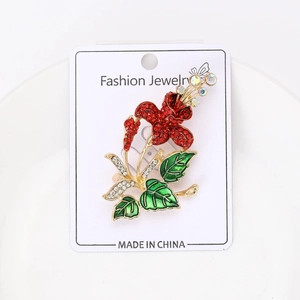 Macro detail of sparkling flower brooch with red rhinestones and green enamel leaf finish
