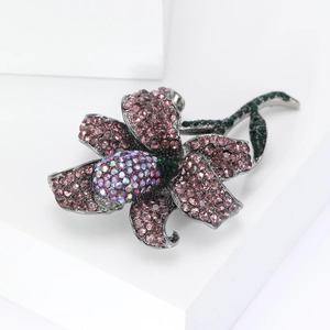 Close-up of a pink rhinestone rose brooch with green leaves on a white background