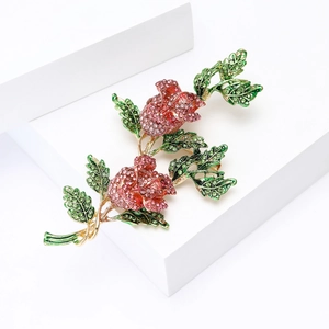 Vue détaillée d'une broche rose sertie de cristaux roses et feuilles en émail vert sur blanc