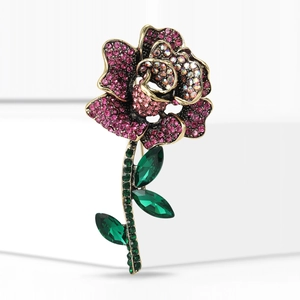 Macro shot of rose brooch with pink rhinestones and green crystal leaves on gold base
