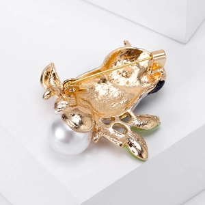 Golden owl brooch back view showing metal texture, safety pin, and white round pearl