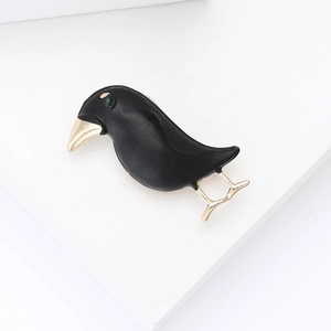 Artistic black enamel raven brooch with golden beak and green gemstone eye on white stand