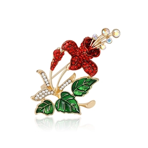 Elegant gold flower brooch with red rhinestones and green enamel on a white background
