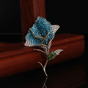Detailed macro of rose flower brooch with blue white crystals and green leaf on golden base