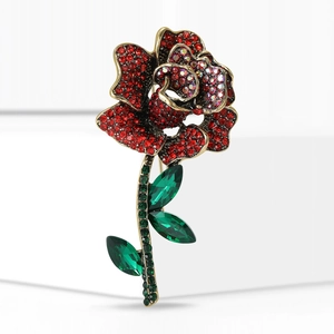 Elegant gold rose brooch with red rhinestones and green crystal leaves on white background