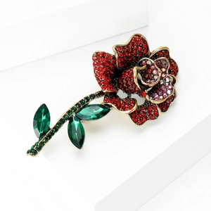 Close-up of luxury rose brooch with red rhinestones and green crystal leaves on white stand