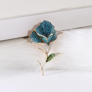Detailed view of an elegant rose flower brooch with blue and white rhinestones on white books