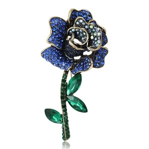 Luxurious rose flower brooch with dark blue crystals and green leaves on white background