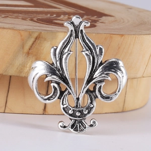 Macro detail of a vintage silver fleur-de-lis brooch on a wooden stand