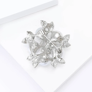Detail view of silver floral brooch with pearls on minimalist geometric white background