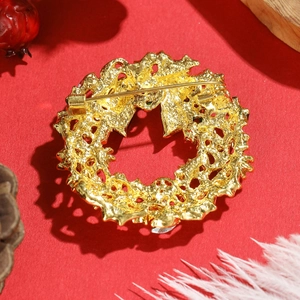 Weihnachtskranz-Brosche aus Goldlegierung mit Anstecknadel auf rotem Hintergrund