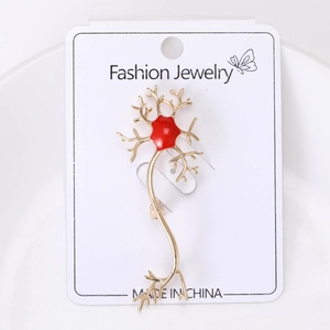 Detailed view of neuron-shaped gold metal brooch with red enamel on display card