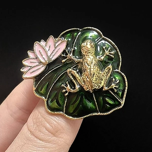 Detailed close-up of a vintage lotus leaf and golden frog enamel brooch pin