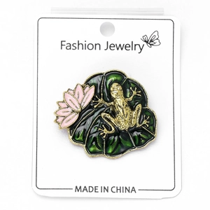 Detailed close-up of a vintage enamel frog brooch sitting on a green lotus leaf