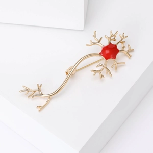 Creative gold-plated neuron cell brooch with red enamel detailing on a white stone background