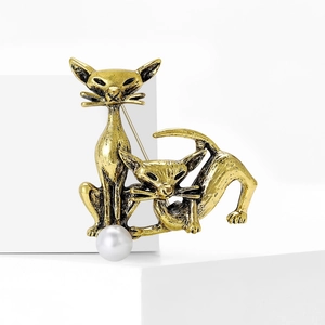 Vintage gold cat brooch with dual cat design and elegant white pearl on a white pedestal