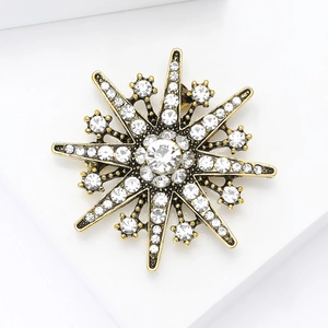 Detailed view of vintage gold snowflake brooch with sparkling crystals on white pedestal