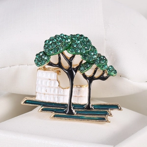 Detailed close-up of a tree brooch with green crystals and enamel on a display pillow