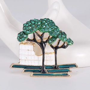 Detail view of a gold-plated tree brooch with green crystals and architecture on a hand model