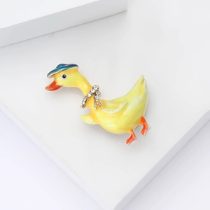 Spilla anatra in smalto giallo con cappello blu e strass luminosi su sfondo bianco puro