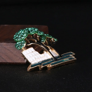 Macro detail of golden tree brooch with green crystals and enamel landscape art