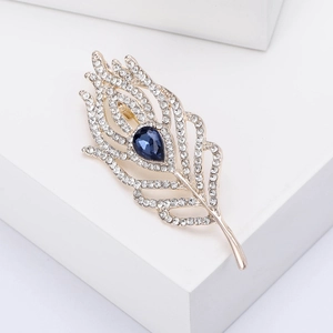 Macro detail of golden feather brooch with white crystals and teardrop blue gemstone