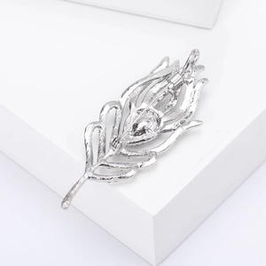 Silver feather-shaped brooch with pin clasp back shown on a white geometric stand