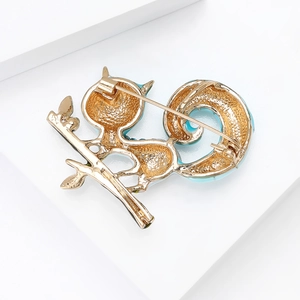 Cute golden squirrel brooch with blue enamel and rhinestones on a green leaf branch