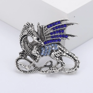 Vintage silver dragon brooch with blue rhinestones on a white geometric display