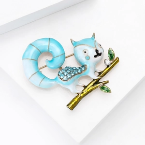 Detail of blue squirrel brooch with rhinestones on a gold branch with green leaves