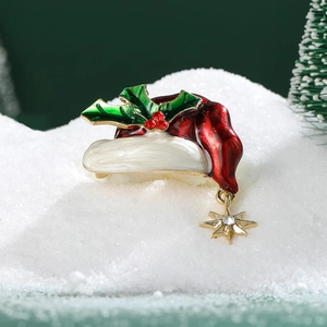 Macro detail of enamel Christmas hat brooch with holly leaves on festive snowy background
