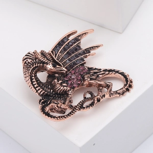 Vintage dragon brooch with bronze metal finish and purple rhinestones on white pedestal